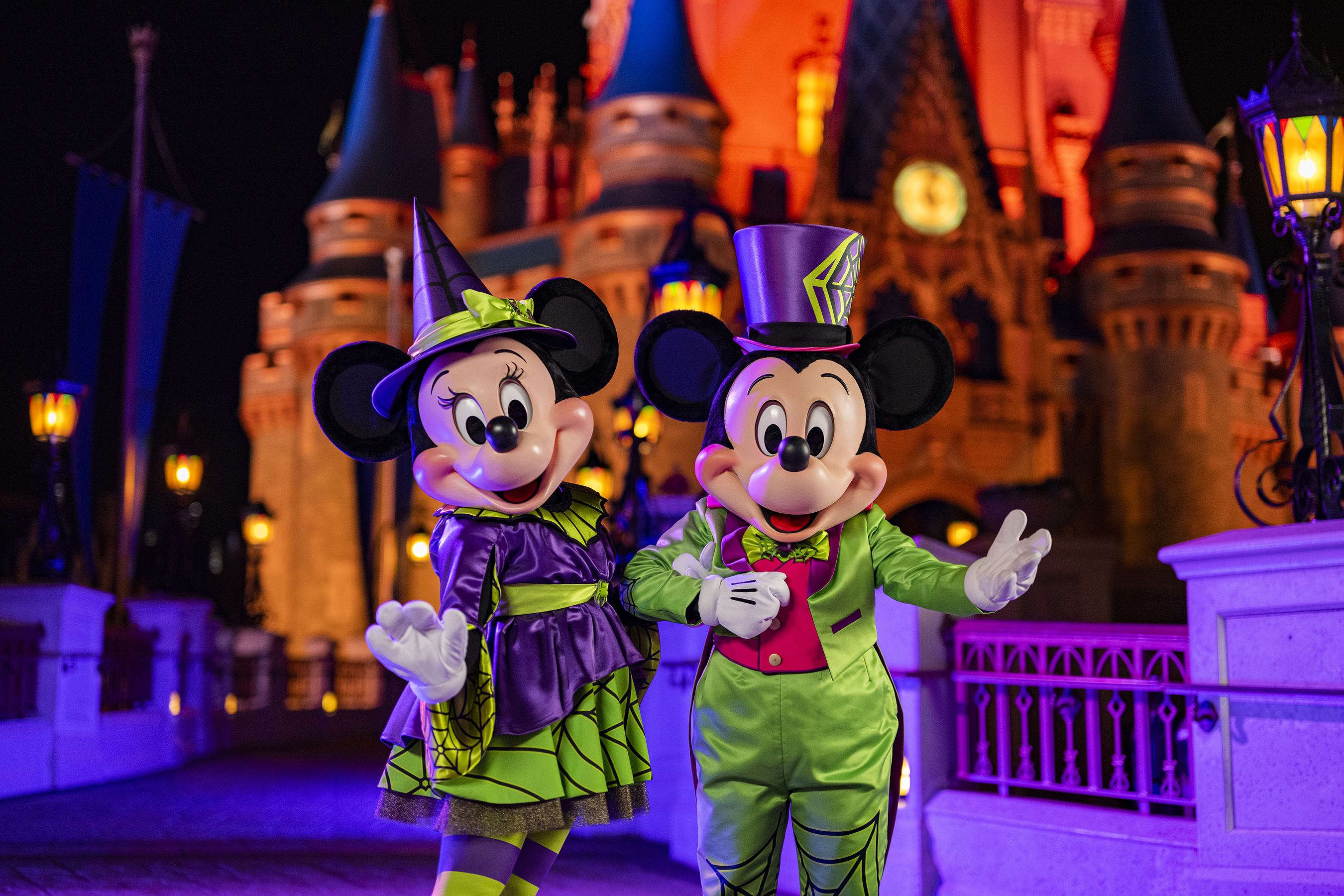 Mickey y Minnie con outfits neón telaraña Halloween frente al castillo iluminado